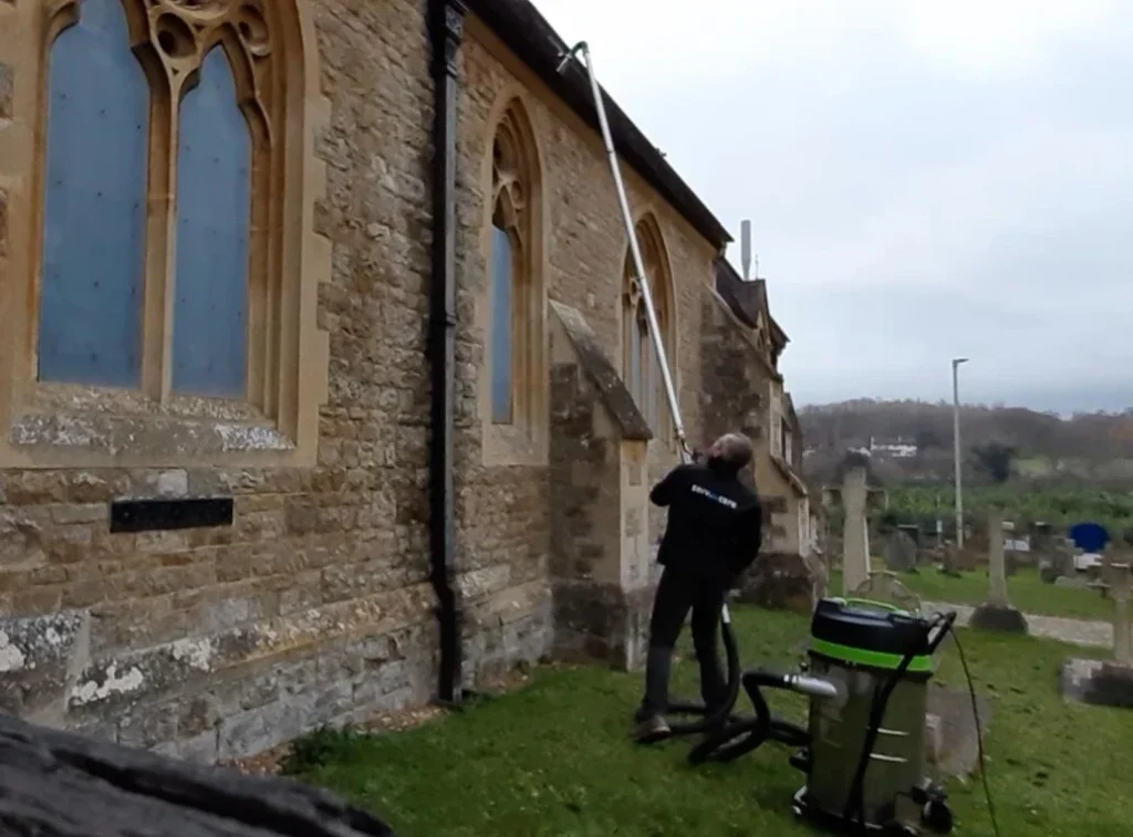 Person cleaning gutter of old stone building