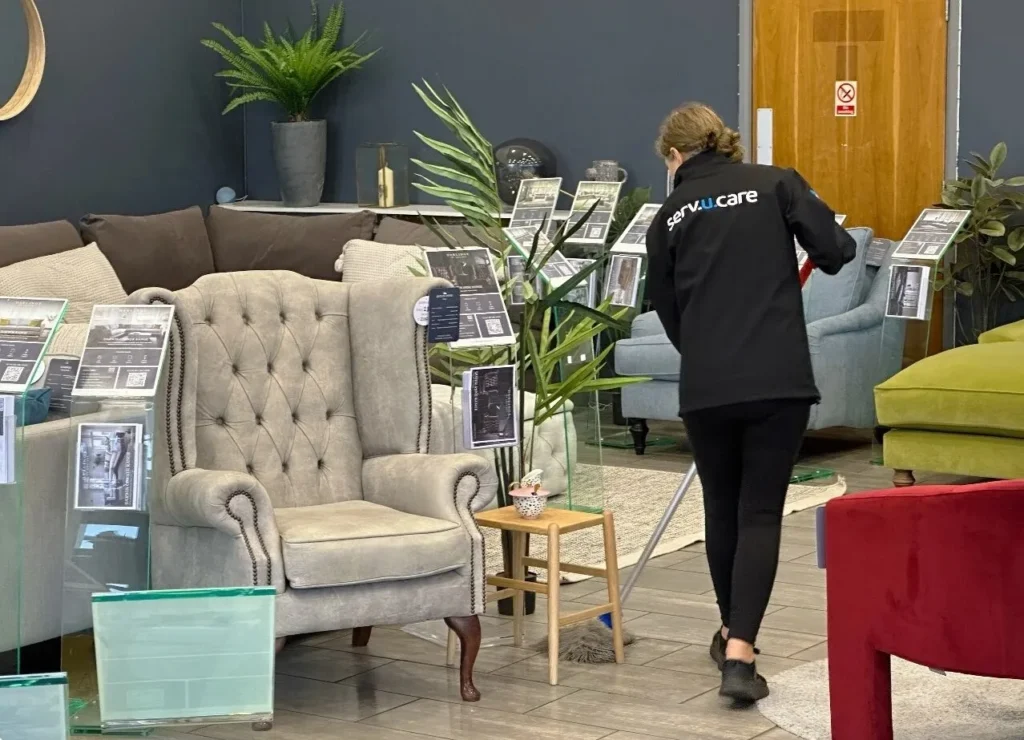 Person cleaning showroom with furniture and plants.